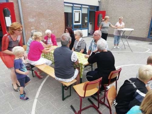 Foto van een groepje ouderen die aan een picknicktafel zitten op het schoolplein.