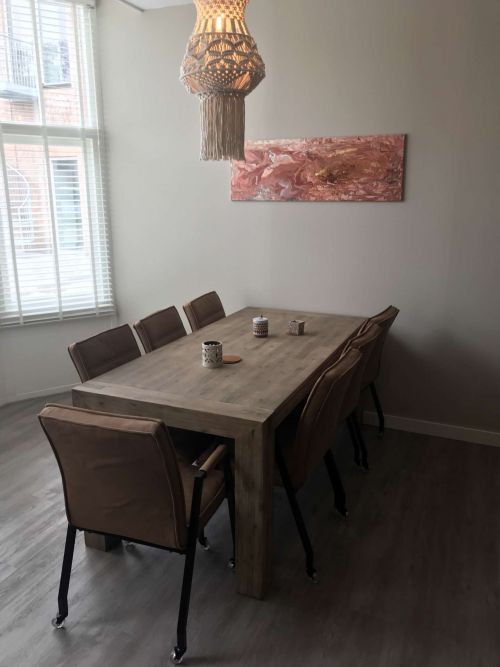 Foto van een rechthoekige tafel met zeven stoelen met een lamp erboven op een houten vloer