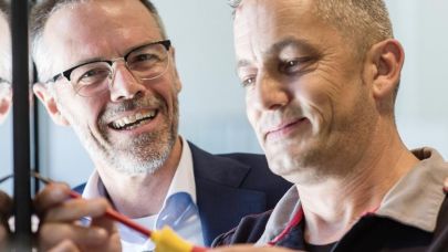 Twee collega's aan het werk waarvan één met een schroevendraaier in de hand Twee collega's aan het werk waarvan één met een schroevendraaier in de hand
