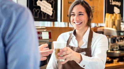 cateringmedewerkster achter de koffiebar die klant een latte aangeeft cateringmedewerkster achter de koffiebar die klant een latte aangeeft