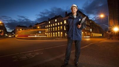 Gebouw in de avond met projectmanager ervoor diebouwhelm draagt Gebouw in de avond met projectmanager ervoor diebouwhelm draagt