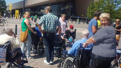Facilicom-medewerkers zijn aan het wandelen met ouderen in een rolstoel, bij centraal station in Rotterdam.