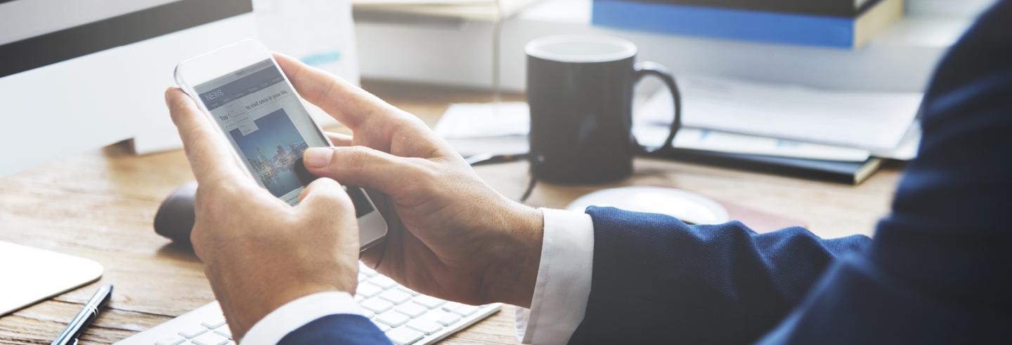 Overzicht van een deel van een bureau met daarboven handen die een mobiele telefoon vasthouden