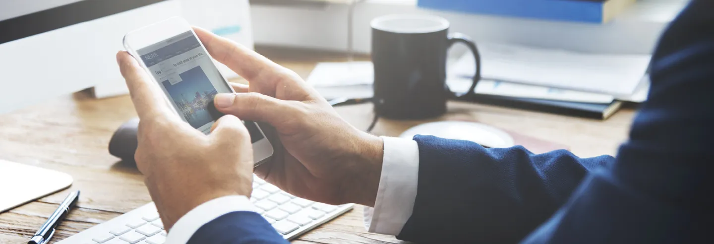Overzicht van een deel van een bureau met daarboven handen die een mobiele telefoon vasthouden