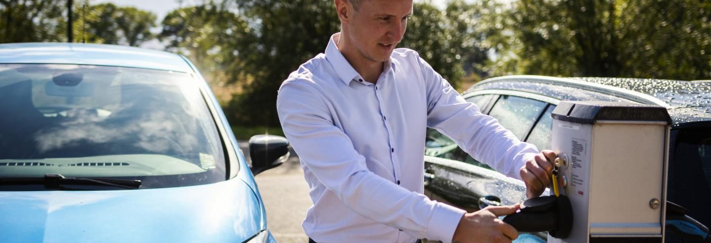 Man sluit zijn auto aan op de stroomvoorziening. De auto is te zien op de achtergrond