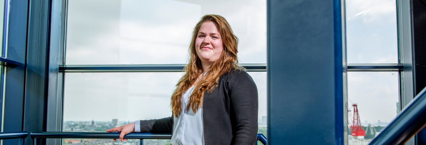 Vrouw staat in trappenhuis op de trap met haar hand op de leuning.