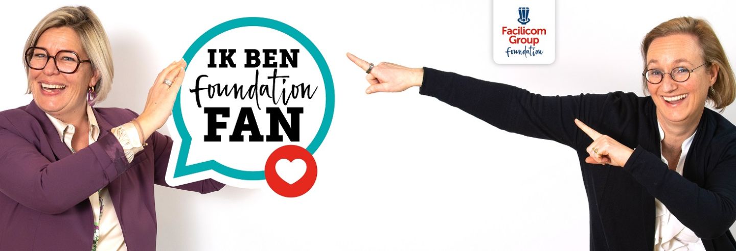 een dame aan de linkerkant die een embleem met de tekst 'Ik ben Foundation Fan' vasthoudt en een dame rechts die met een 'dab' ernaar toe wijst.