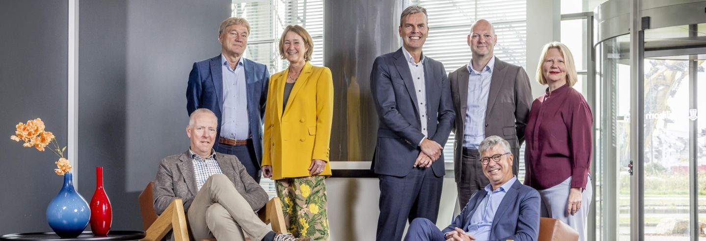 Een zevental personen, 2 vrouwen en 5 mannen die lachend in de camera kijken