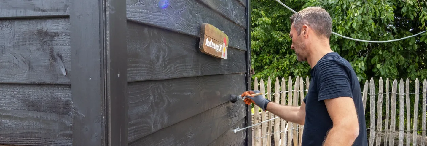 Een collega staat een schuur te verven
