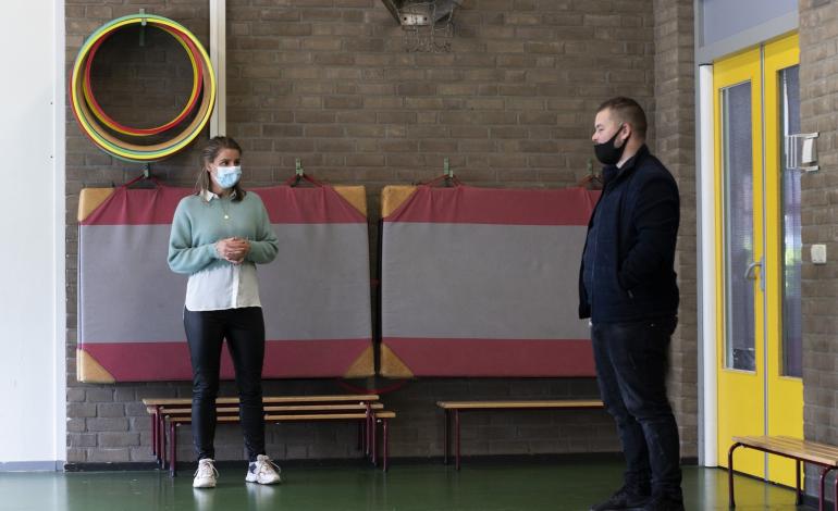 Diede Smit staat in een gymzaal te praten met een vrijwilliger van Stichting Grote Broer.